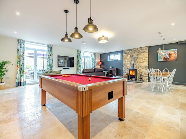 A pool table in a well-lit room with a stone wall, a fireplace, and a dining area.