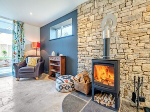 A living room with a stone wall, a fireplace, a leather chair, a wooden cabinet, and a window with curtains.