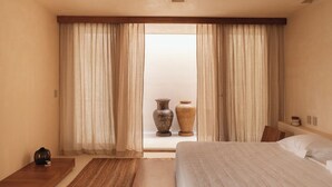 Een ruime slaapkamer met een groot bed, houten vloer en uitzicht door dunne gordijnen.