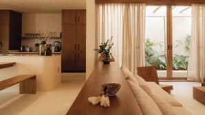 Een moderne keuken met houten kastjes, een eethoek met een lange houten tafel, en uitzicht op groen door grote schuifdeuren.