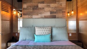 A bed with patterned pillows, a headboard with a textured design, and wooden paneling on the walls. - Los Muertos Beach Walking Distance Suite - C406 (Puerto Vallarta)