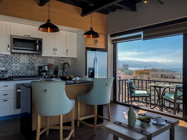 Una cocina moderna con una isla grande, taburetes de bar y vistas a la ciudad y montañas a través de un ventanal.