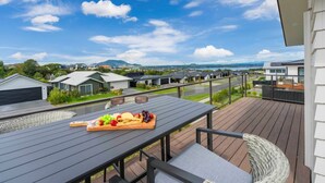 Un balcón con una mesa de madera dispuesta para una comida, con vista a una zona residencial con casas modernas y un cielo despejado.