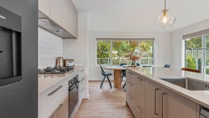 Cocina moderna con horno, estufa y pileta integrados. Cuenta con un comedor, una mesa y sillas, y un amplio ventanal con vistas al exterior.