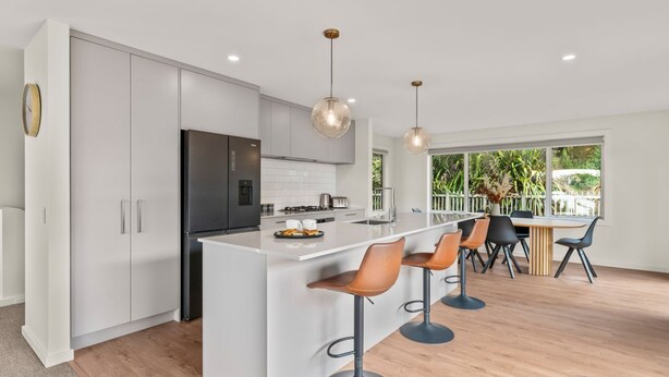 Una cocina moderna con una isla central, taburetes de bar y un comedor con vista a zonas verdes.