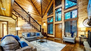 A log cabin interior with a staircase, leather sofas, a coffee table, and a fireplace. - Simmer Down: Shuffleboard, Pool Table, Hot Tub, Firepit, Sleeps 17 (Broken Bow)