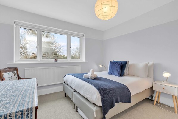 A bedroom with a bed, bedside table, nightstand, window, and a table with a patterned tablecloth. - Artist Haven With Parking By My Getaways (Brighton)