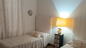 A bedroom with two single beds, a nightstand with a lamp, and a wall clock. - Villa Teresa (L´Ametlla de Mar)