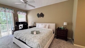 Un dormitorio con cama, escritorio, silla, mesita de noche, lámpara y ventilador de techo.