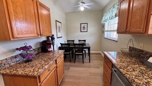 Une cuisine dotée de meubles en bois, de plans de travail en granit, d’une table à manger avec des chaises et d’un ventilateur de plafond.