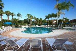 Un área de piscina con sillas de descanso y sombrillas, rodeada de palmeras.