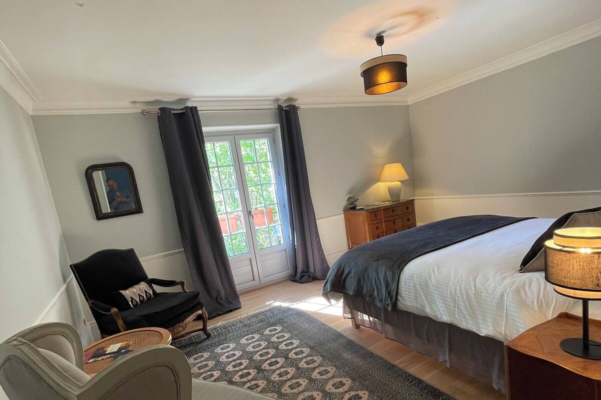Une chambre à coucher comprenant un lit, une chaise, un bureau, une lampe et une vue sur l’extérieur.
