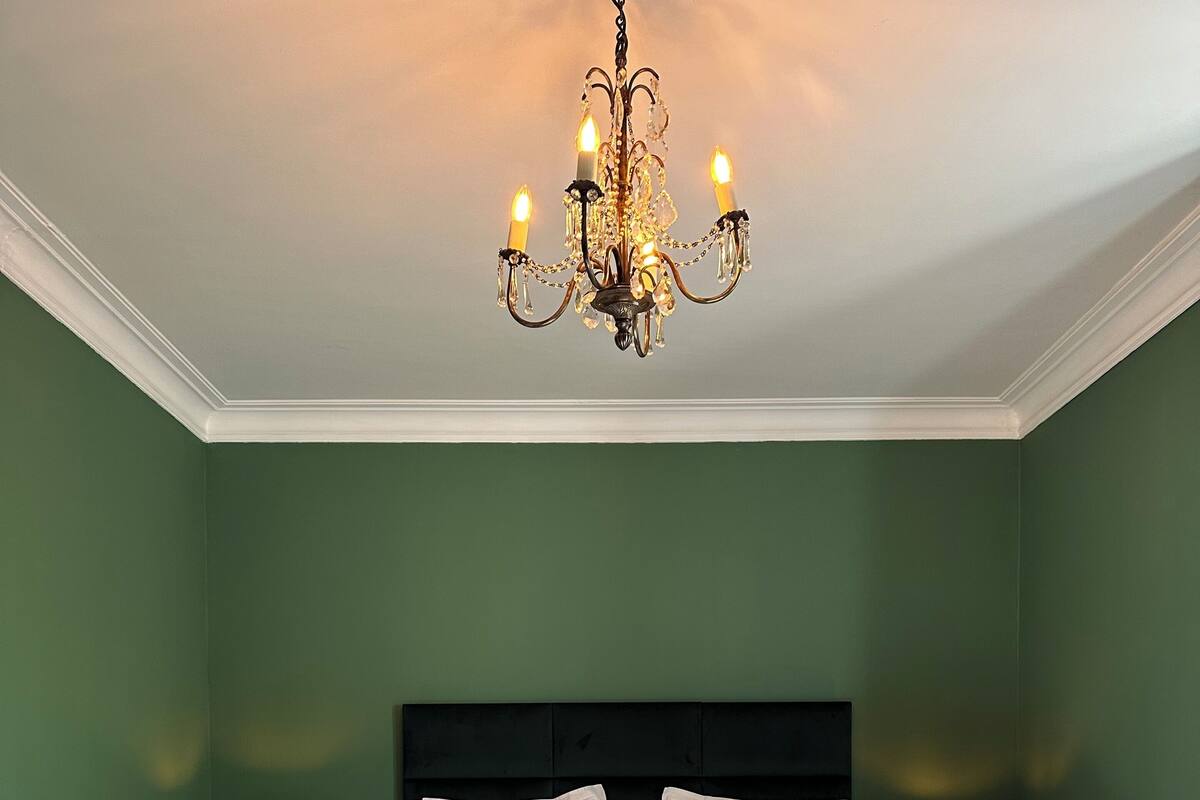 Une chambre à coucher avec un grand lit, deux tables de chevet, un lustre et des murs verts.