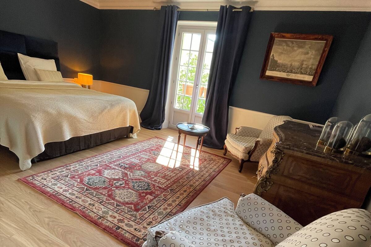 Une chambre à coucher comprenant un lit, une chaise, une petite table, une commode et un lustre.