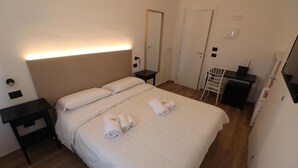 A hotel room with a bed, a bedside table, a desk, a chair, a mirror, and a wardrobe. - Hotel Noto Marina Vista Mare (Noto)