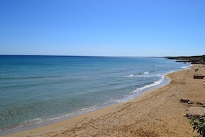A beach with clear blue water, sandy shore, and a few scattered rocks. - Hotel Noto Marina Vista Mare (Noto)