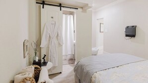 Ein Schlafzimmer mit einem Bett, einem Nachttisch mit Lampe, einem an der Tür hängenden Bademantel und einem an der Wand montierten Fernseher.