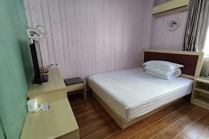 A bedroom with a bed, a desk, a chair, a nightstand, and a wall-mounted air conditioning unit.