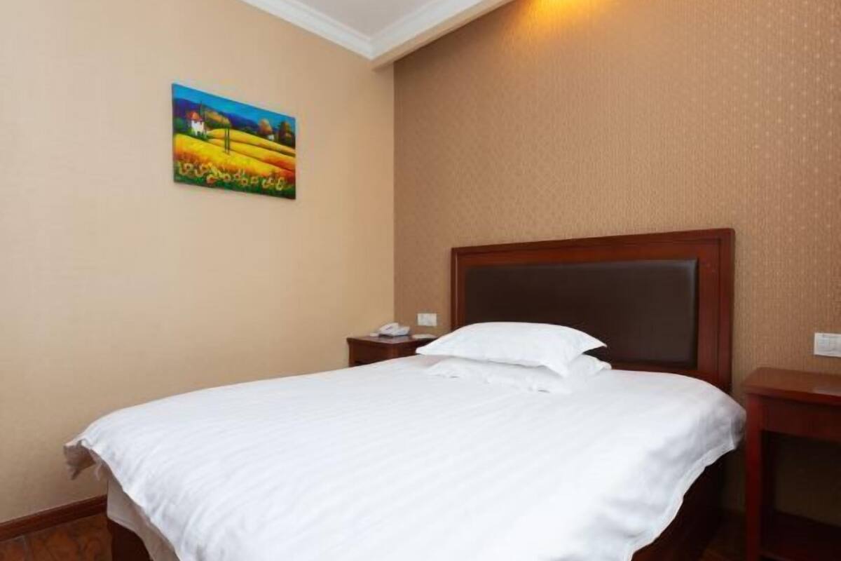 A hotel room with a neatly made bed, a nightstand with a phone, and a painting on the wall.