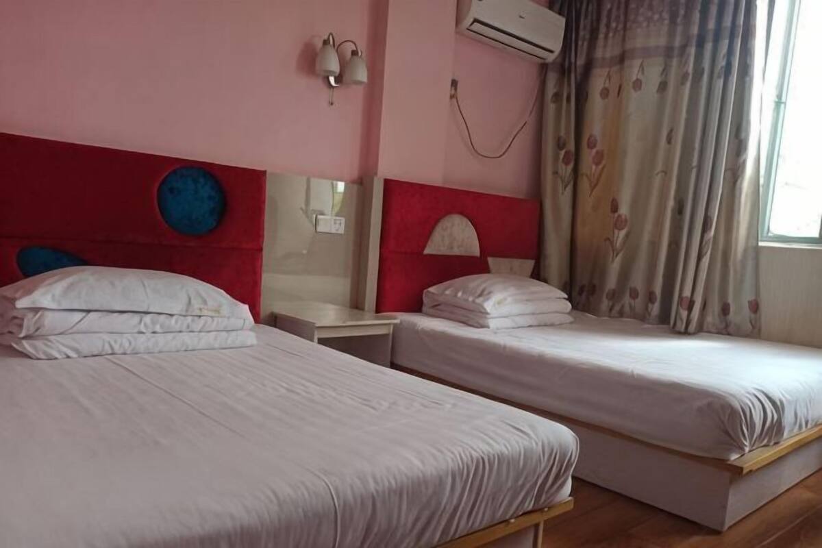 Two single beds with white bedding, a red headboard, a wall-mounted air conditioner, a mirror, and a window with curtains.