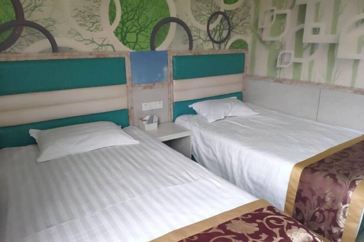 A room with two beds, each with white bedding and a headboard. The room has a green and white color scheme with a tree pattern on the wall.