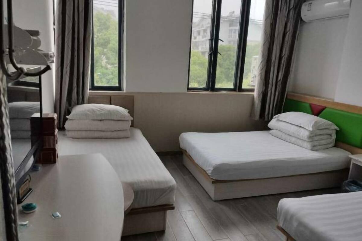 A hotel room with two single beds, a bedside table, a mirror, and a window with curtains.