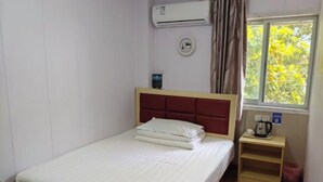 A single bed with a red headboard, a bedside table with a kettle, and a window with curtains.
