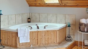 Un plafond en bois avec une lucarne, une baignoire en bois, une serviette blanche, une petite table avec une bougie et un tapis à motifs.