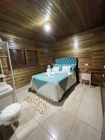 A bedroom with a wooden ceiling, a bed with a blue headboard, a nightstand, and a white fluffy rug.