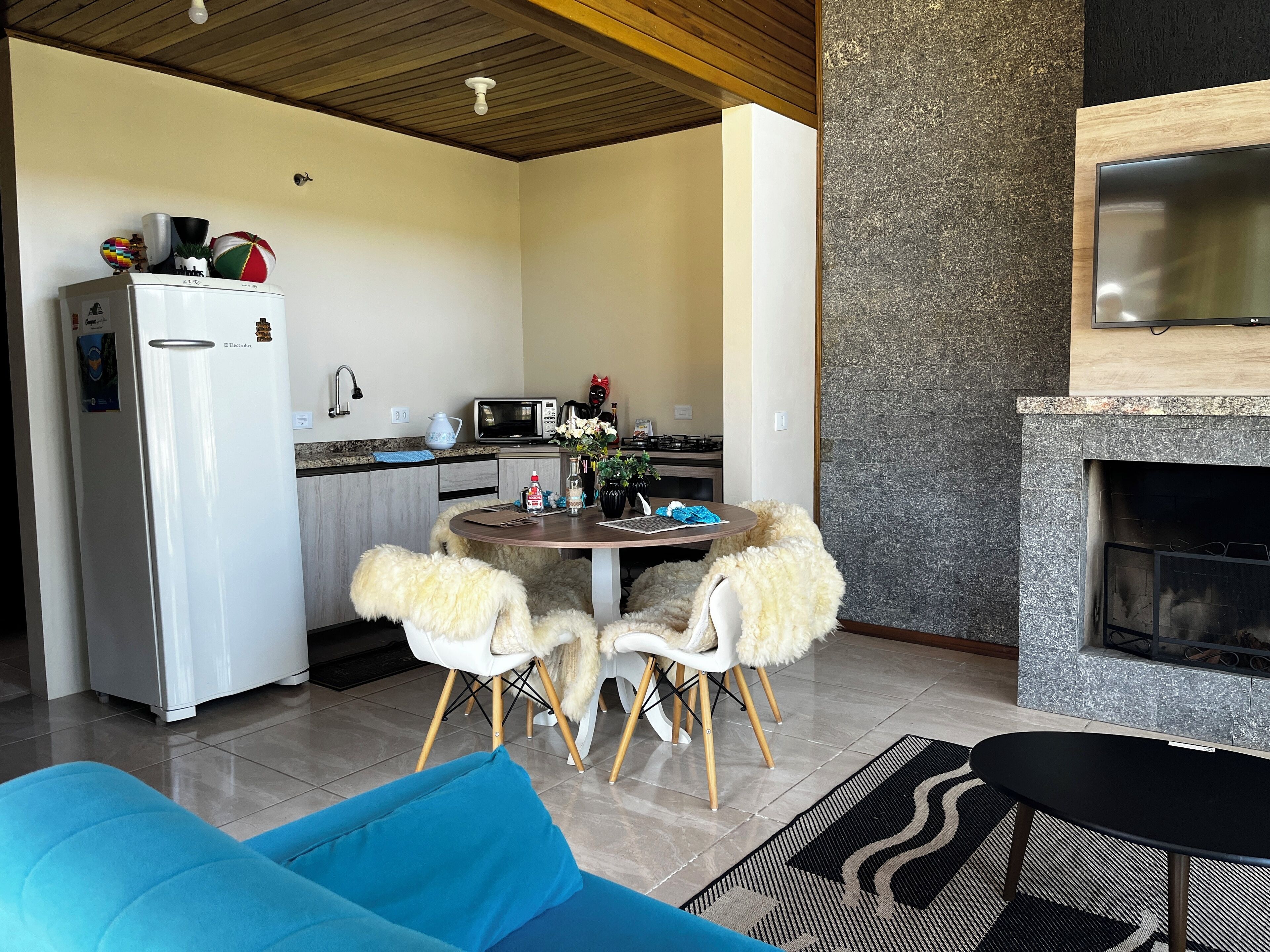 A modern kitchen with a refrigerator, microwave, and stove. There is a dining area with a round table and two chairs. A fireplace is visible in the background.