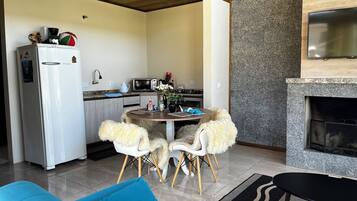A modern kitchen with a refrigerator, microwave, and stove. There is a dining area with a round table and two chairs. A fireplace is visible in the background.
