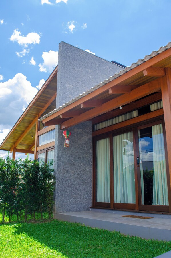 A modern house with a sloped roof, large glass windows, and a wooden porch. - Canyons Guest House (Praia Grande)