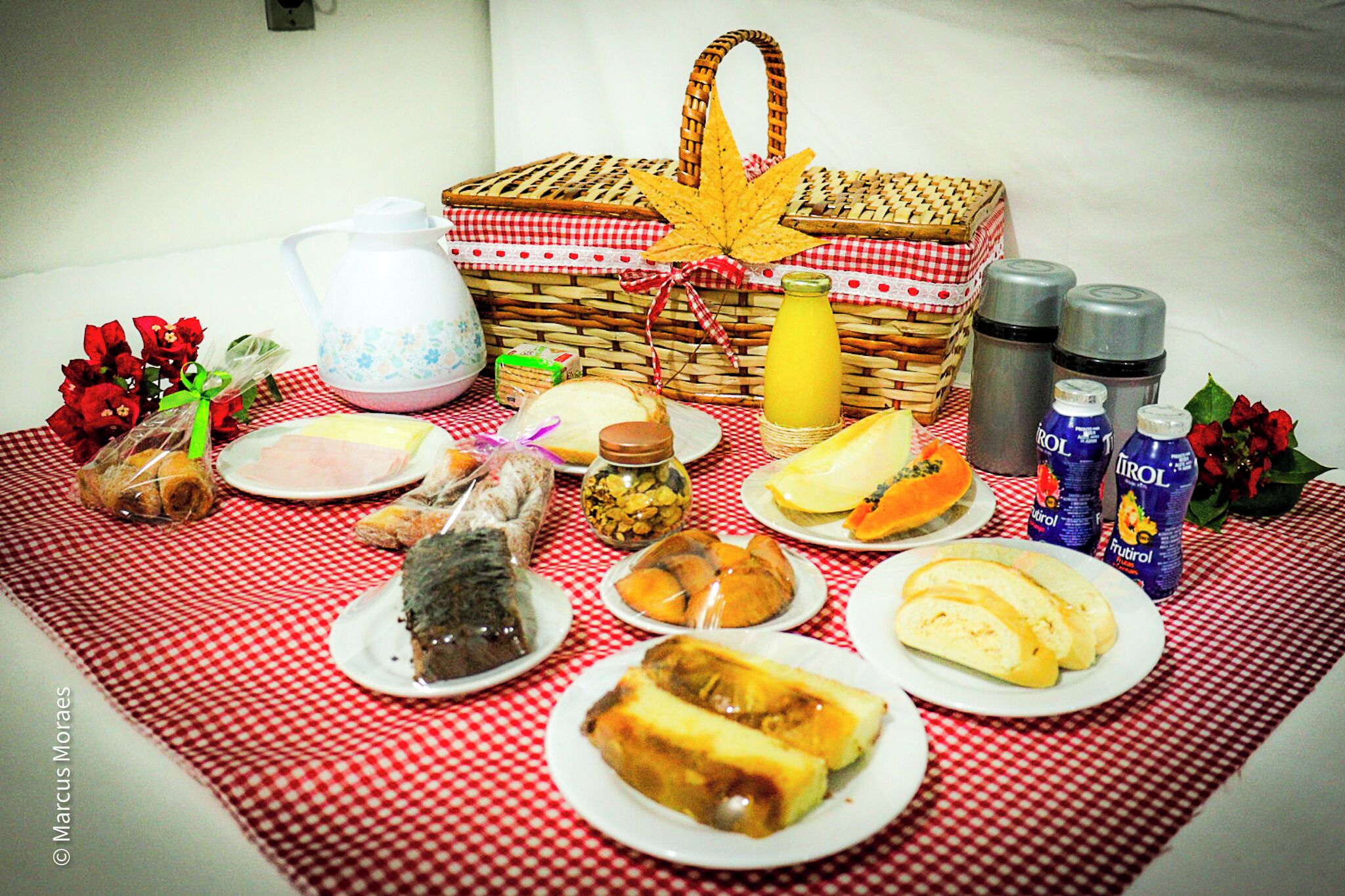 Ein Picknickdeko mit kariertem Tischläufer, einem Korbwägelchen und verschiedenen Speisen, darunter Brot, Gebäck und Früchte.