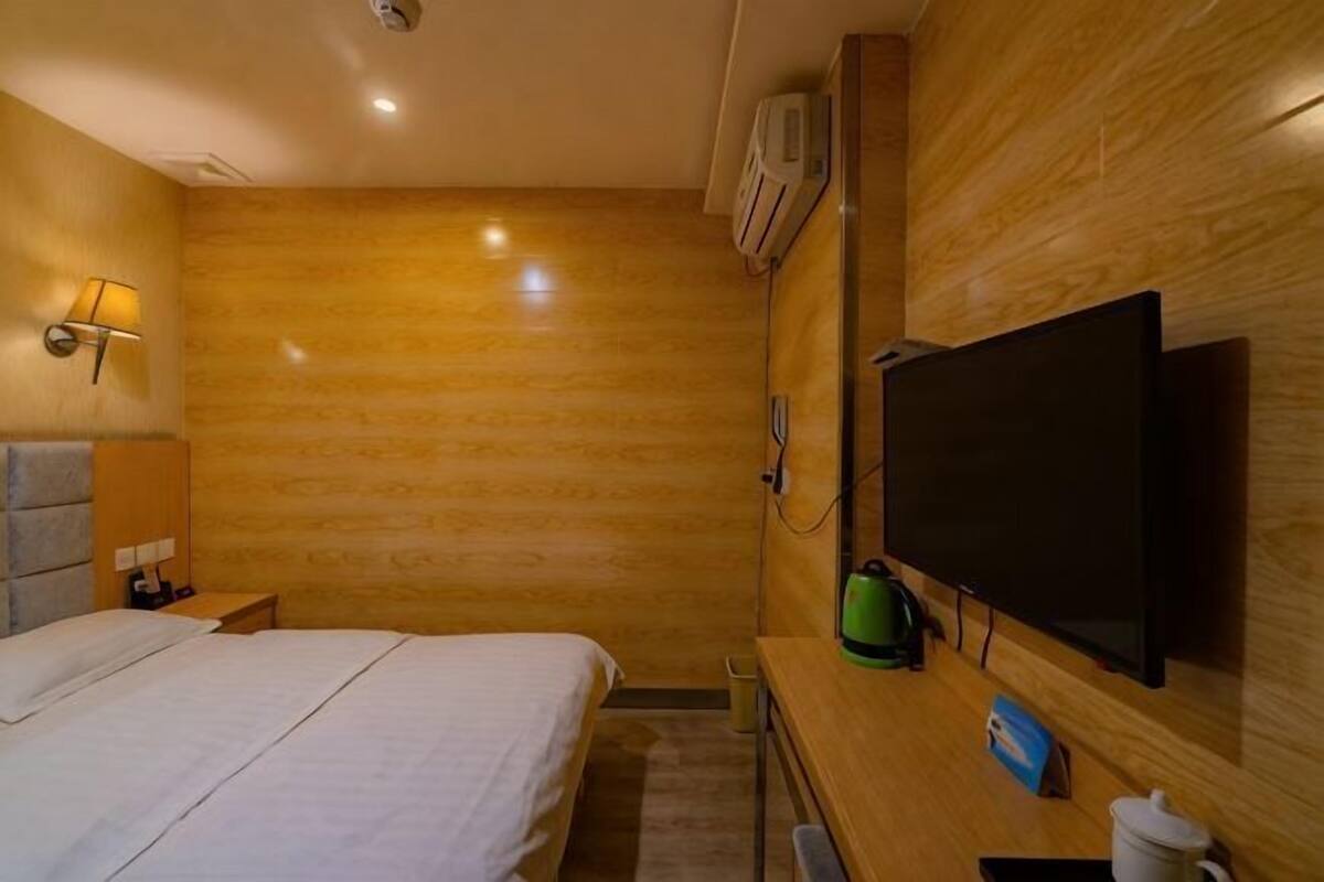 A hotel room with a bed, bedside table, lamp, TV, and wooden wall paneling.