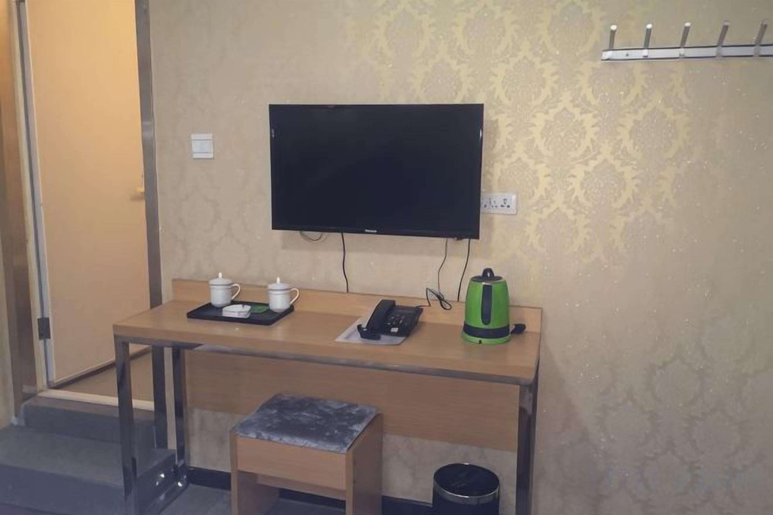 A hotel room with a desk, a television, a kettle, and a trash bin.