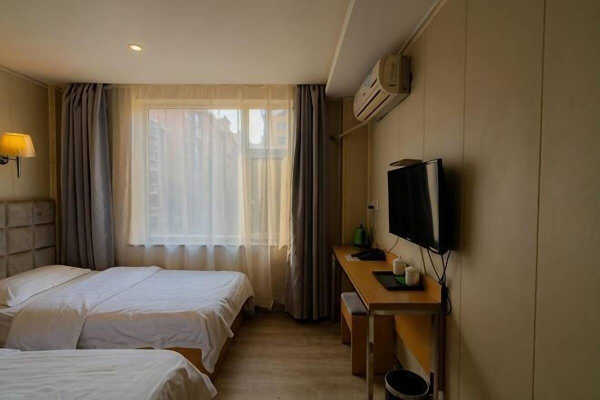 A hotel room with two beds, a desk with a television, and a window with curtains.