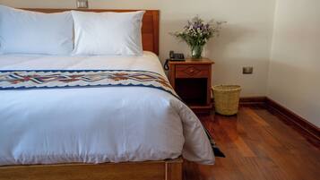 Una cama bien tendida con una colcha estampada, un cabecero de madera, una mesita de noche con un jarrón de flores y una cesta de mimbre.