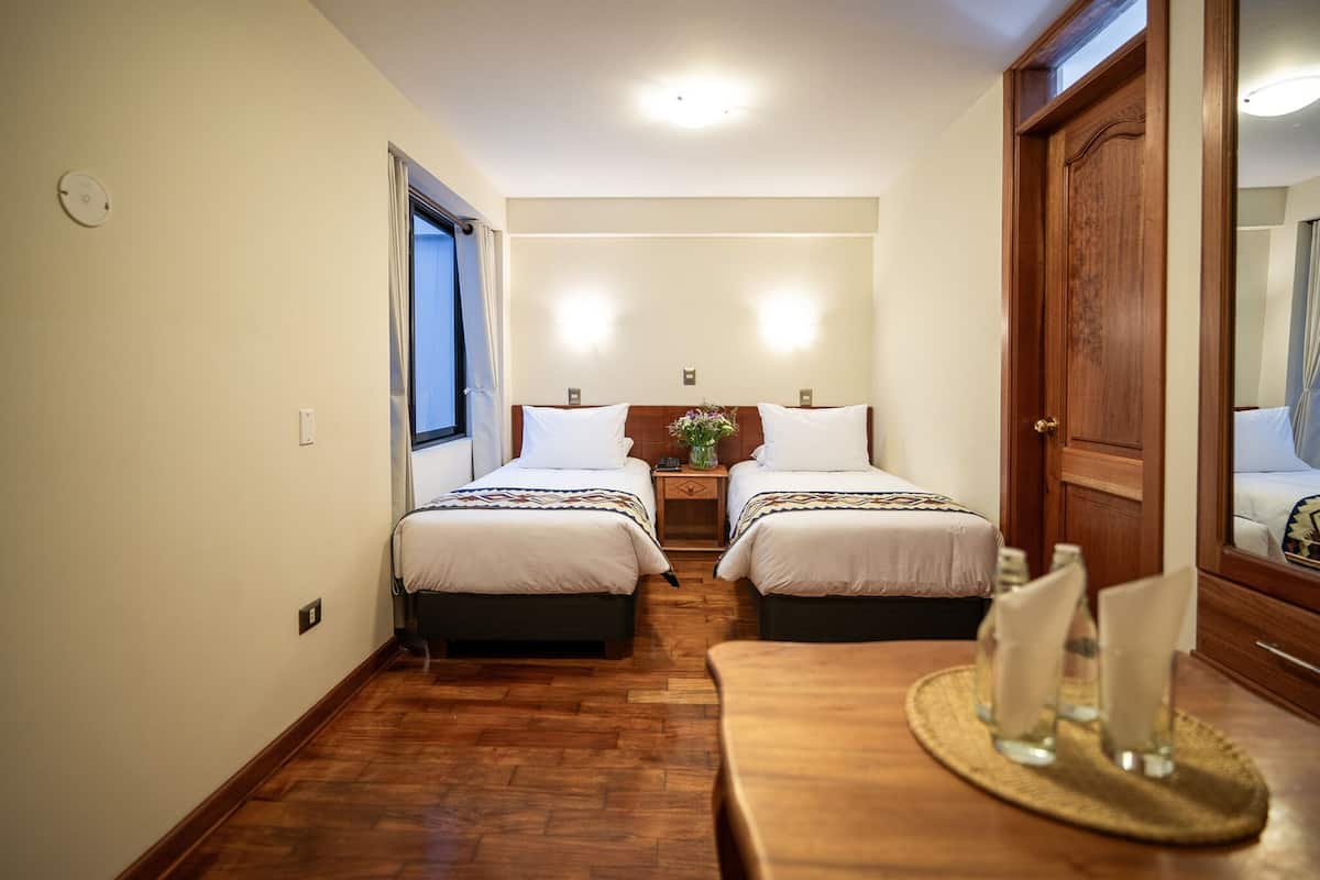 Une chambre d’hôtel avec deux lits, un plancher en bois, une table à manger avec des serviettes et un grand miroir.