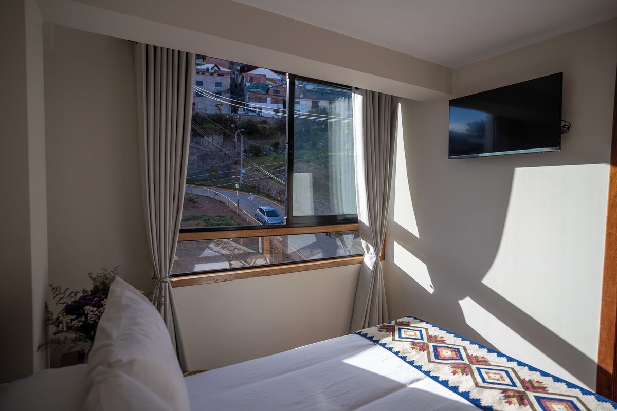 A hotel room with a bed, a TV mounted on the wall, and a window with curtains.