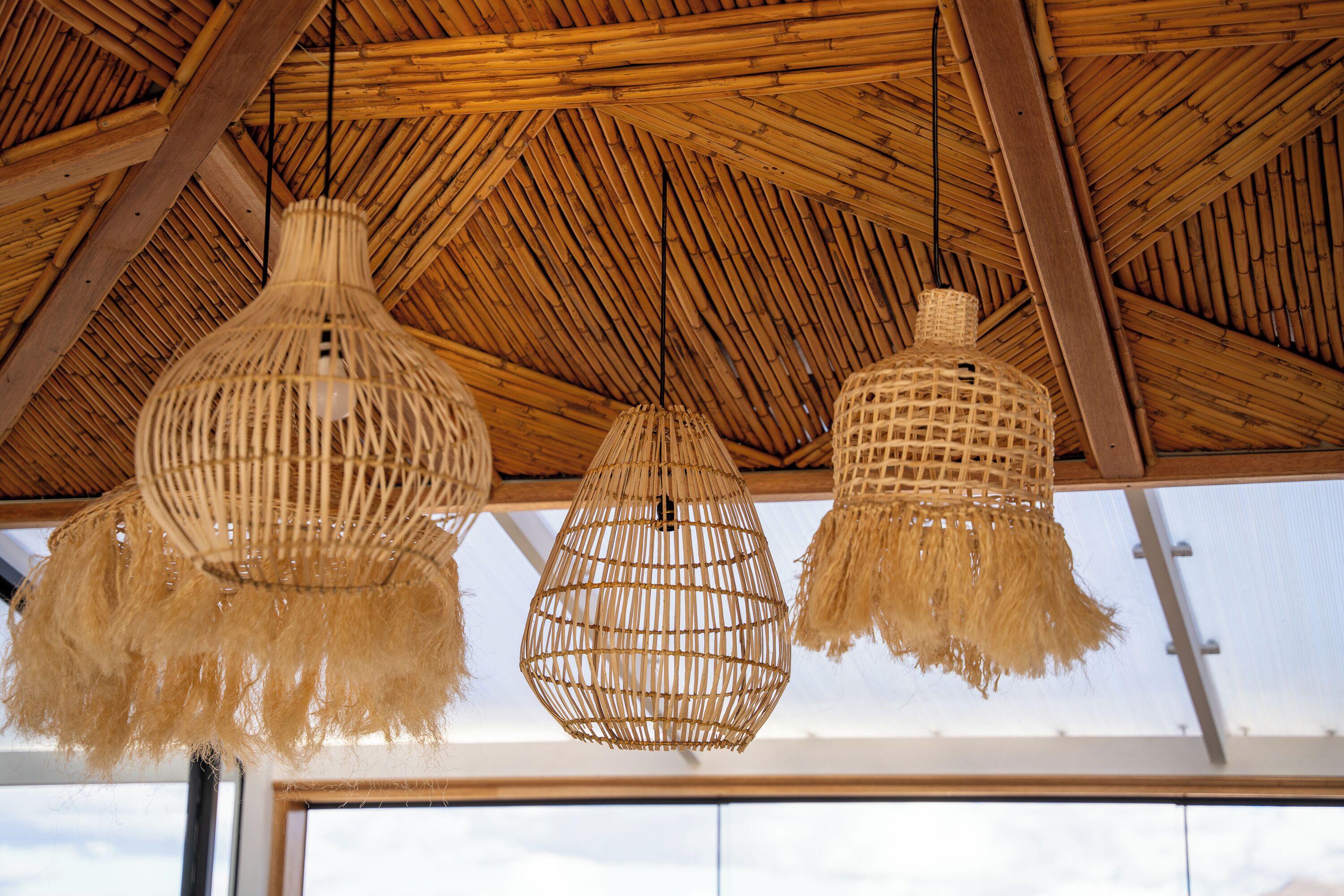 A ceiling with woven bamboo beams and three hanging light fixtures.