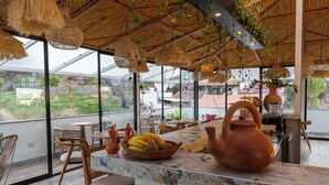 A modern dining area with a large window, wicker ceiling, and a central table with a fruit bowl and teapot. - Cavana Hotel Boutique Cusco (Cusco)