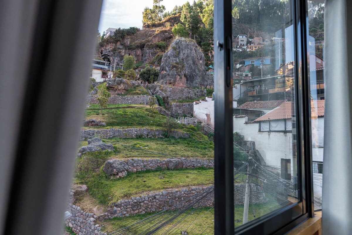 A view of terraced fields and a rocky hill with buildings in the background.