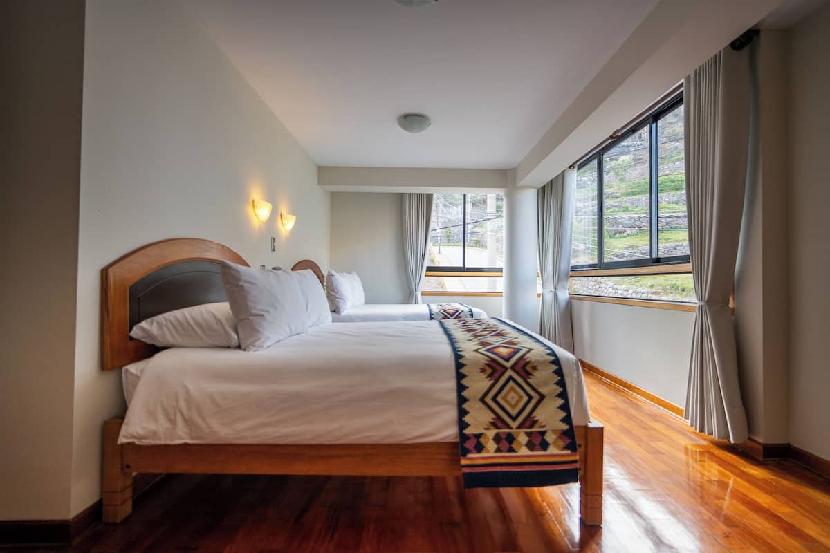 Une chambre d’hôtel avec deux lits, une grande fenêtre avec des rideaux, un plancher en bois et un luminaire au plafond.