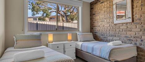 A bedroom with two beds, a brick wall, a window, and a mirror.