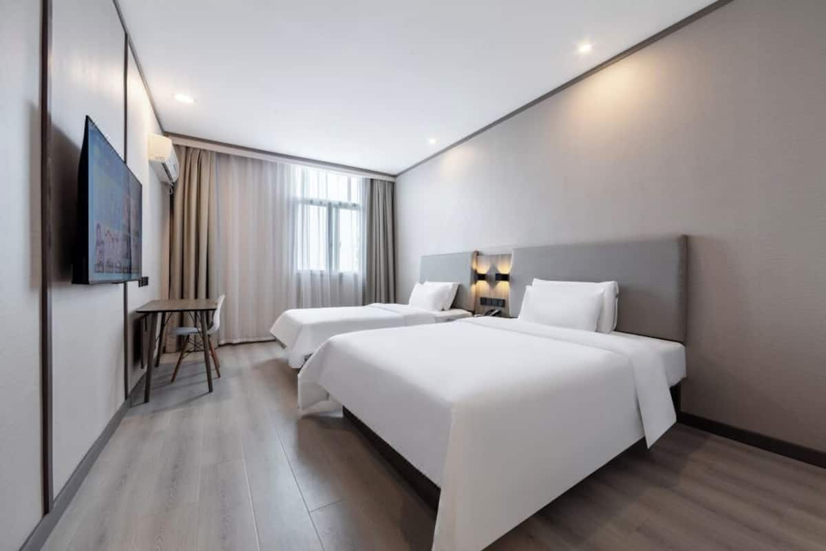 A hotel room with two beds, a desk, a TV, and a window with curtains.