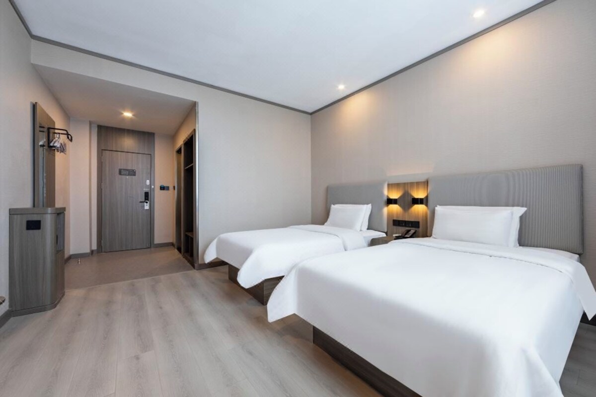 A hotel room with two beds, a wardrobe, a desk, and a nightstand with lamps.
