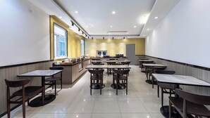 A spacious cafeteria with multiple tables and chairs, a central counter with food items, and a large window on the left. - Hanting Hotel Shanghai Hongqiao Airport Beidi Road (Shanghai)