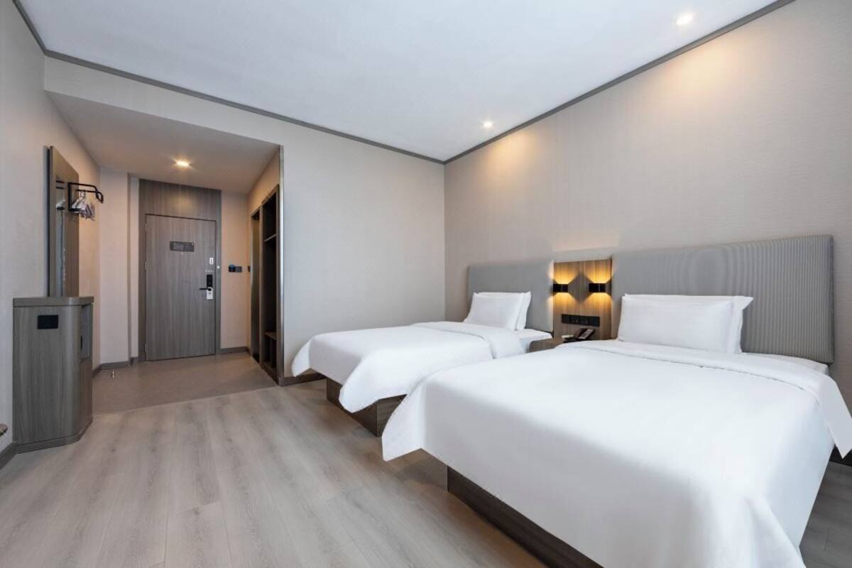 Ein Hotelzimmer mit zwei Betten, einem Kleiderschrank, einem Schreibtisch und einem Nachttisch mit Lampen.