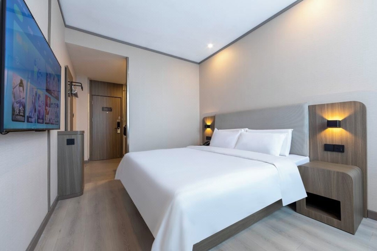 A hotel room with a large bed, bedside lamps, a wall-mounted TV, and a door leading to another room.