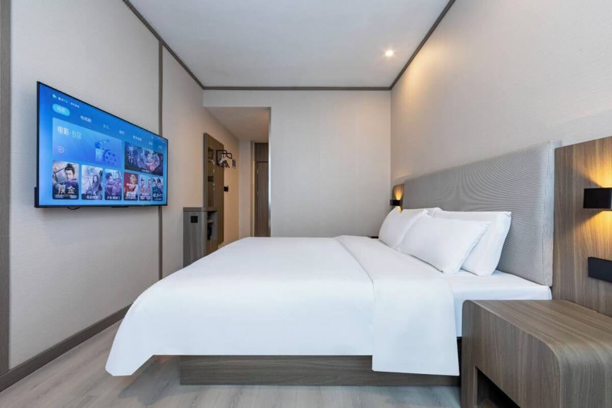 Ein modernes Hotelzimmer mit einem großen Bett, einem flachbildfernseher an der Wand und einem Nachttisch aus Holz.
